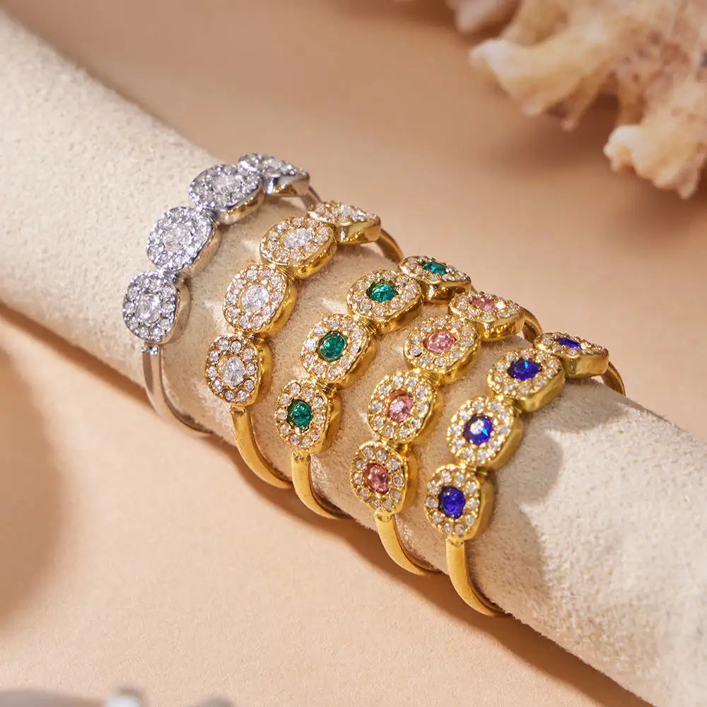 A collection of elegant, pave-set bangles in gold and silver tones featuring colorful gemstones like emerald, sapphire, ruby, and amethyst.