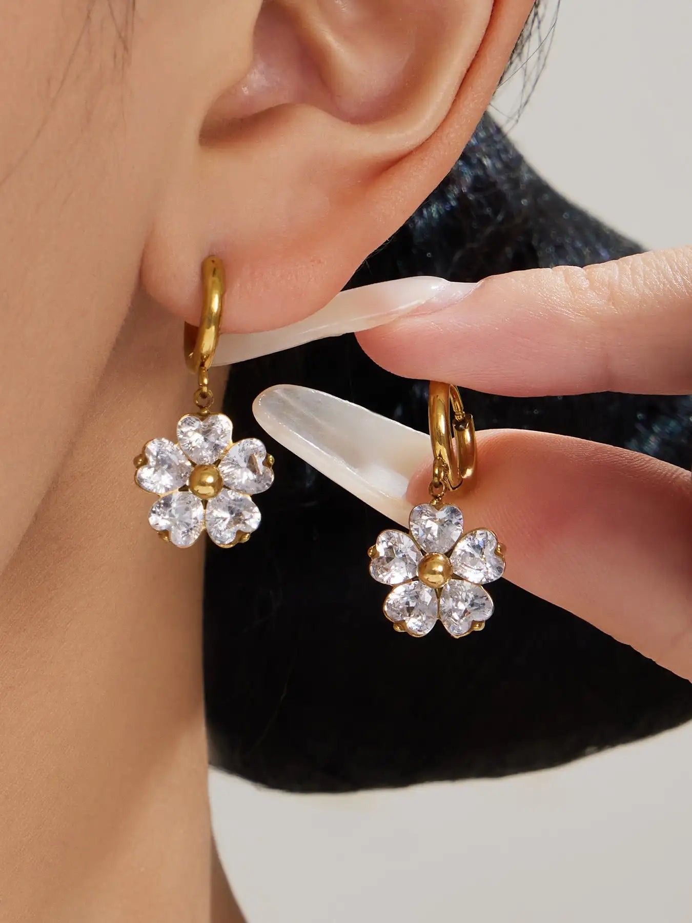 Gold-toned hoop earrings featuring a delicate five-petal flower design with clear, faceted crystals and a central gold accent.