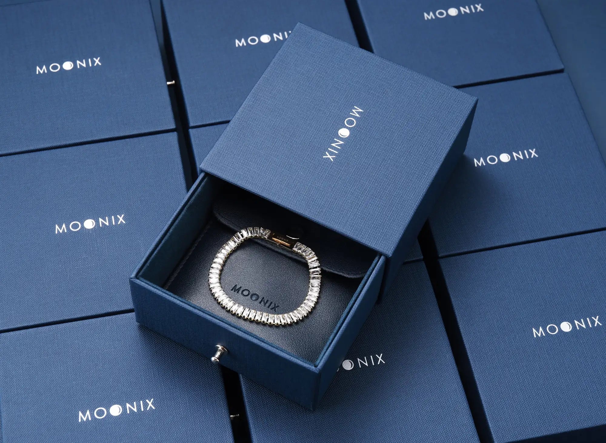 A silver-toned, textured bracelet with a sleek, modern design rests elegantly inside a navy blue moonix gift box.