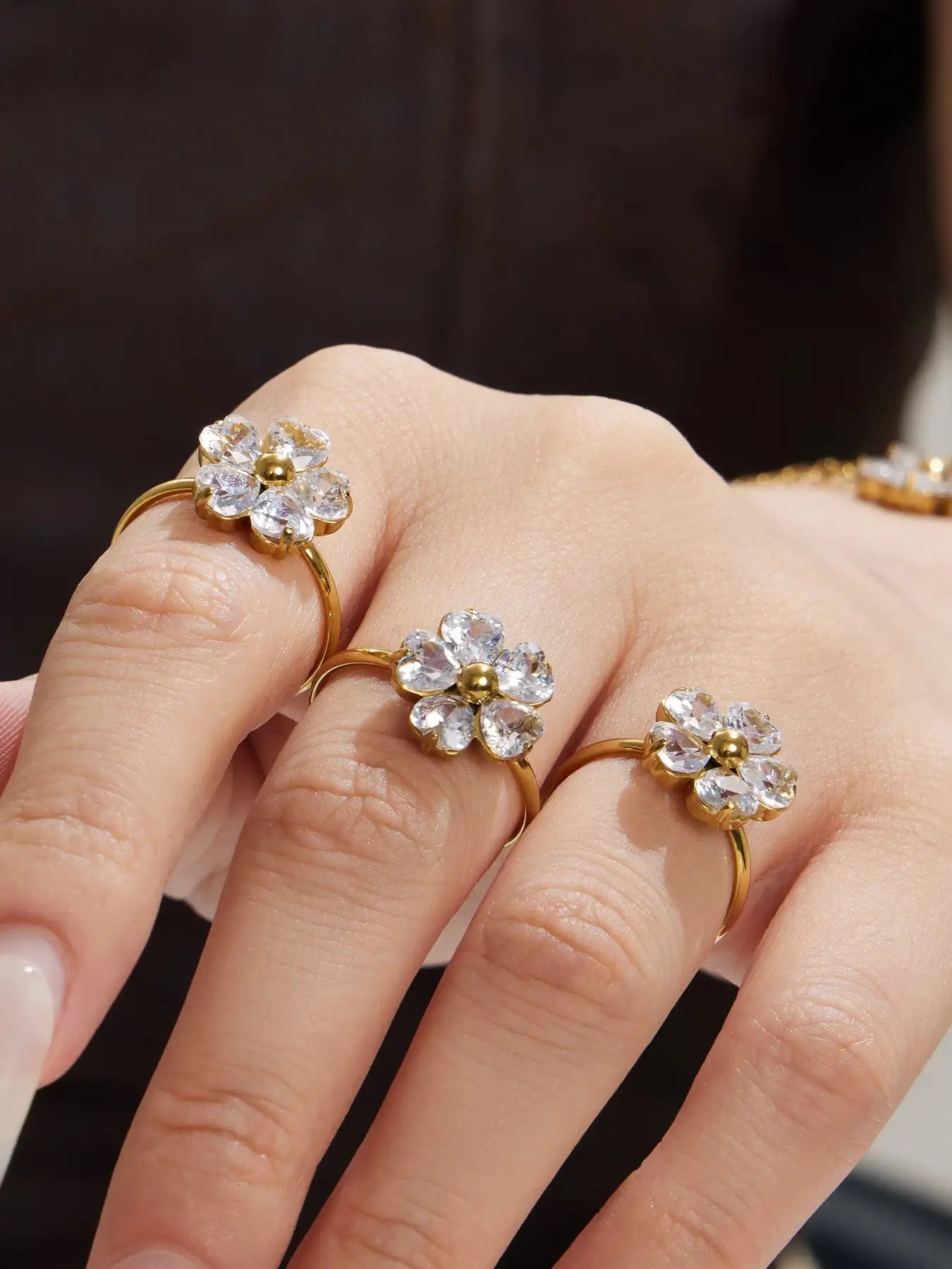 Three delicate gold-toned flower rings, each featuring a central golden bead surrounded by clear crystal petals.