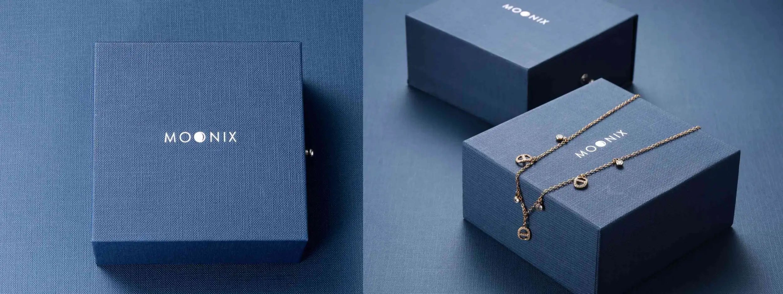 A delicate gold-toned chain necklace with small circular charms and a larger pendant, displayed on a navy blue moonix gift box.